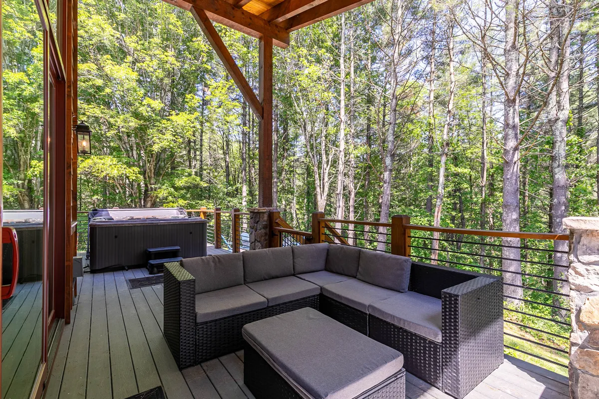 A picturesque outdoor seating area nestled among tall pine trees, featuring a spacious hot tub and comfortable seating. The area is designed for group relaxation and is surrounded by natural greenery, offering sweeping mountain views and a tranquil escape. The setting is ideal for enjoying both quiet mornings and lively evening gatherings.