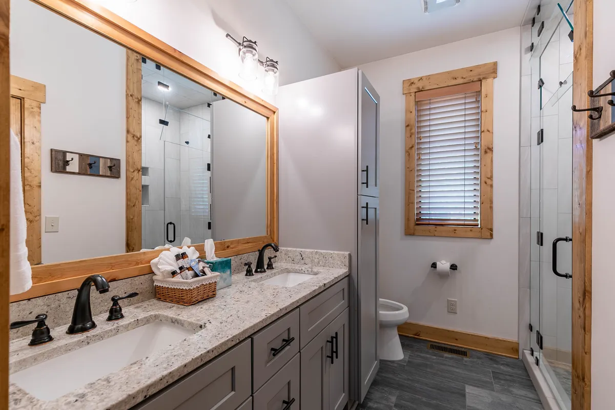 A stylish bathroom with a double sink vanity, large mirror, walk-in shower, and warm wooden accents. The space feels spa-like and serene, ideal for private self-care routines.