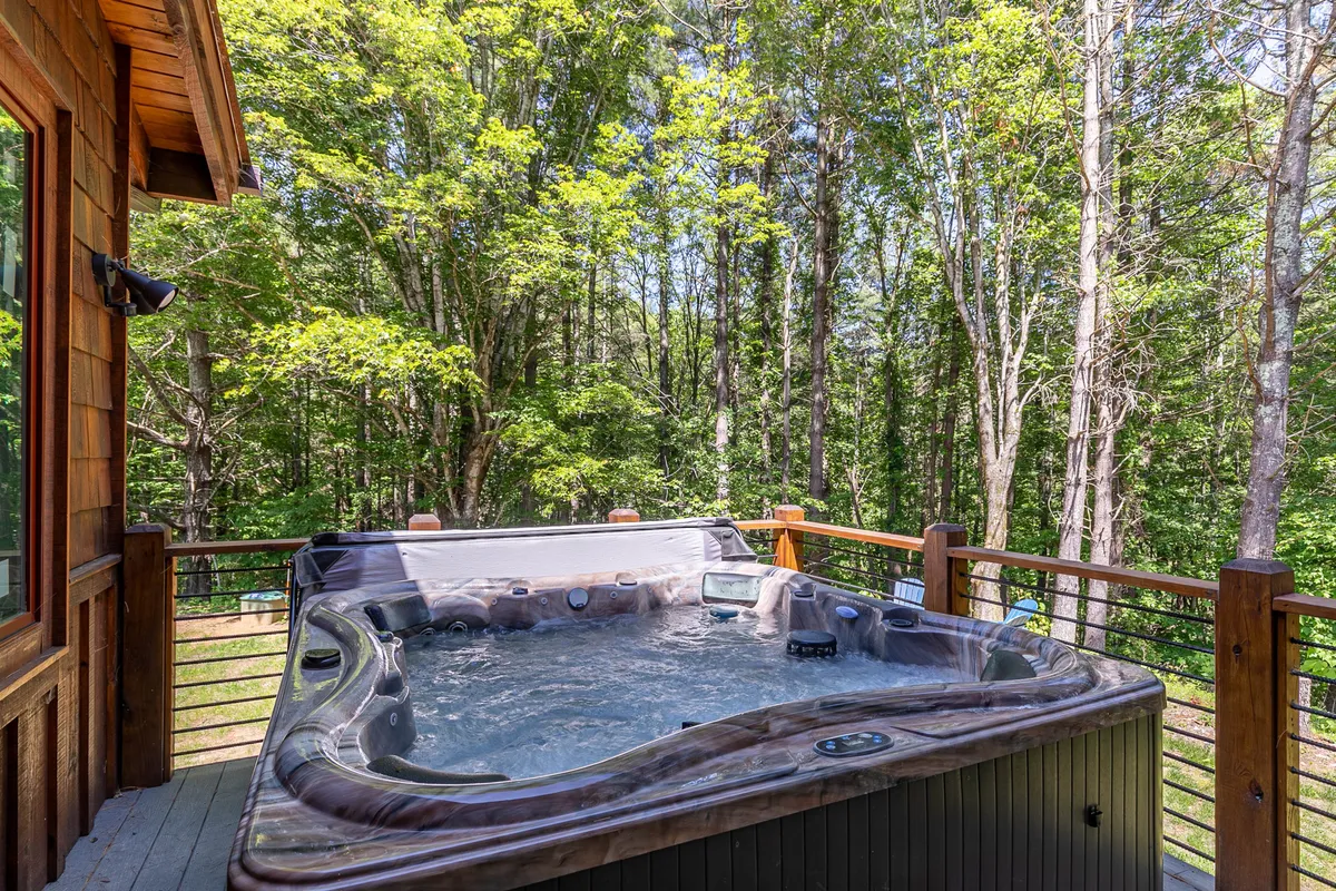 A serene exterior shot showing a private hot tub on a wooden deck, surrounded by lush greenery. The inviting setting suggests relaxation after a day full of adventure, with room for families or small groups to unwind and enjoy nature together.