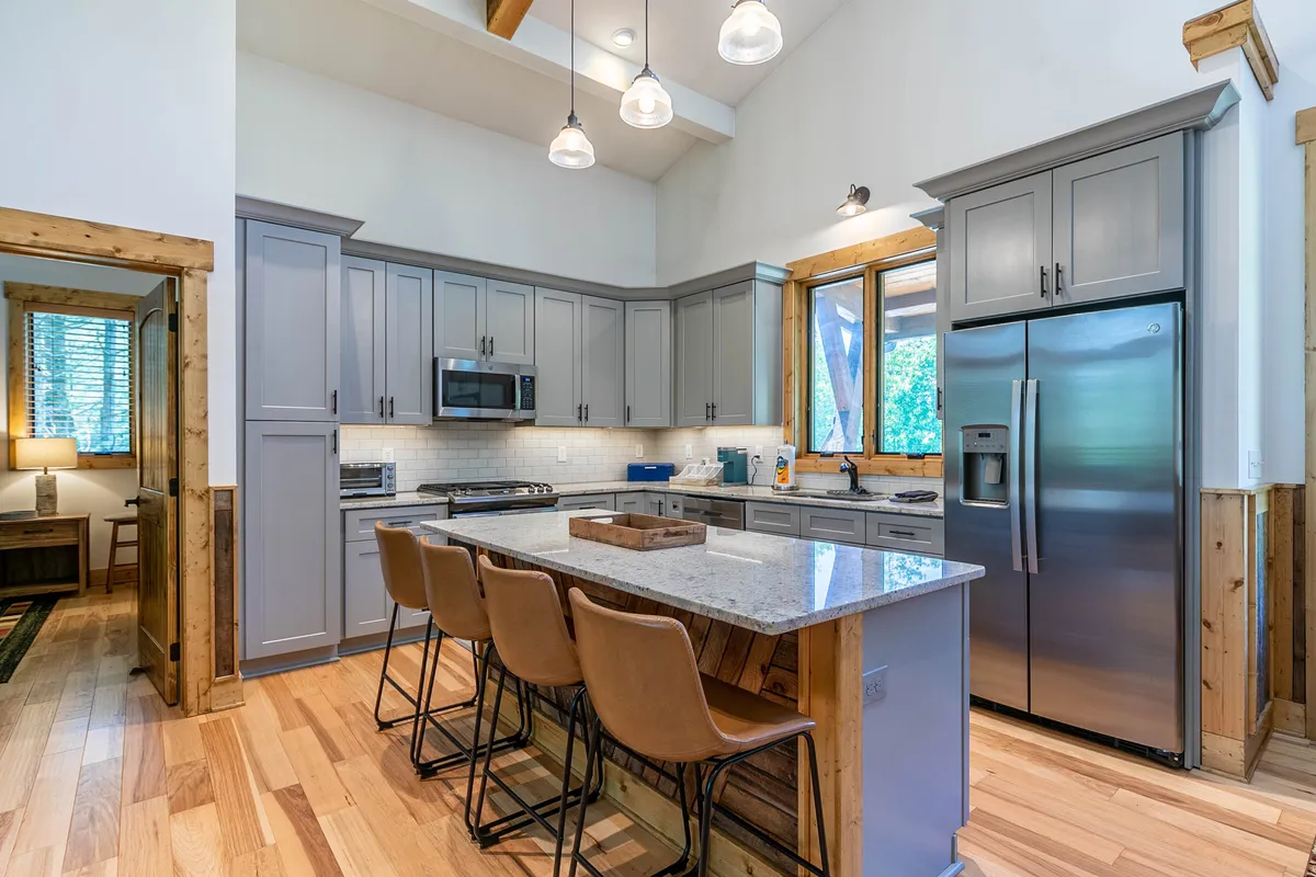 The image showcases a modern kitchen with a large island, stainless steel appliances, and wooden cabinetry. The space is ideal for group activities like cooking, entertaining, and sharing meals, with a welcoming and functional design.