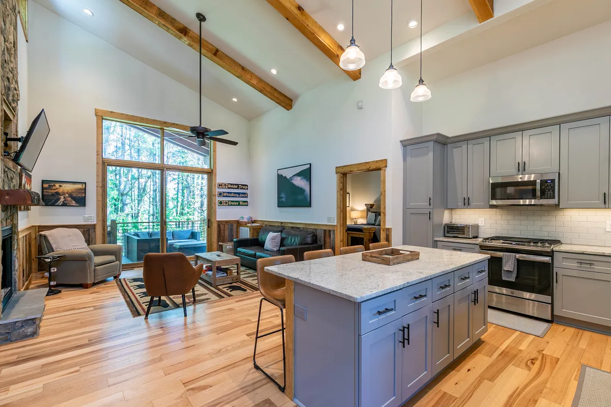 A spacious open-concept living area that seamlessly connects the modern kitchen, dining area, and cozy living room. The focal points include a kitchen island, an inviting electric fireplace, large windows that bring in natural light, and a plush seating area perfect for relaxing or entertaining guests.