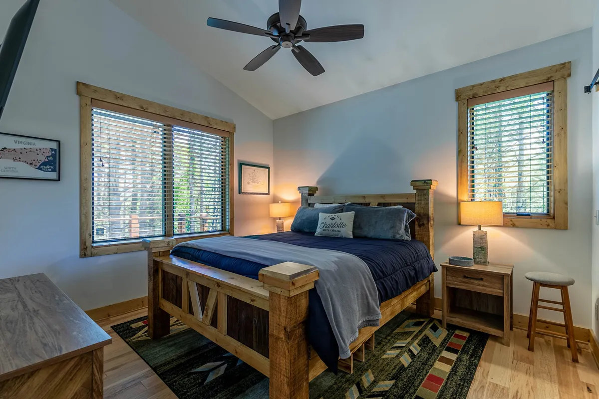 A cozy bedroom with a wooden bed frame, decorative pillows, table lamps, and a rug with geometric patterns. Gentle natural light fills the space, enhancing the room's comfort and restful feeling.