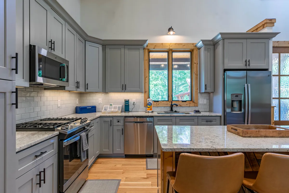 A modern kitchen with sleek appliances, granite countertops, wooden accents, and large windows. The kitchen is inviting and perfectly suited for family meals, socializing, or preparing treats, with natural light enhancing the space's warmth.